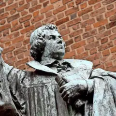 Statue eines Mannes mit Buch und erhobener Hand vor Ziegelwand. Ein Denkmal, das an den Reformationstag in Schleswig-Holstein erinnert.