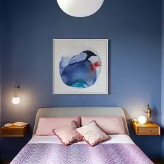 Camera da letto con pareti blu intenso e un quadro astratto. Letti con cuscini rosa e una coperta viola creano colori rilassanti.