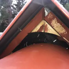 Detaljbild av taknock med vindskiveplåt och trädetaljer.