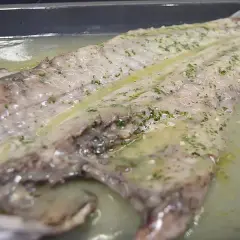 Lubina salvaje preparada en una bandeja con salsa de limón y hierbas, lista para cocinar.