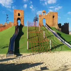 Un castillo de juguete con toboganes y red de escalada en un parque de las familias.