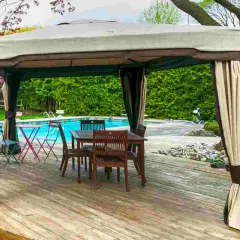 Gazebo su terrazza in legno, con tavolo e sedie, vicino a una piscina. Soluzione per come fissare un gazebo su terrazza senza bucare il pavimento.