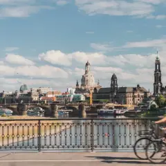 Two people enjoy bike tours in Germany, cycling across a bridge with a scenic view of Dresden's historic skyline.