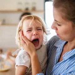 Mama próbuje uspokoić dwulatka, który przeżywa histerię. Dziecko głośno płacze, mama trzyma je czule.