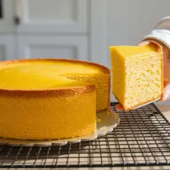 Una fetta di torta allo yogurt, soffice e dorata, viene sollevata da una tortiera intera.