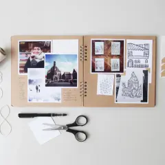 Oto przykład, co to jest scrapbooking: otwarta księga z przyklejonymi zdjęciami, rysunkami i notatkami, obok nożyczki, pisak i sznurek.