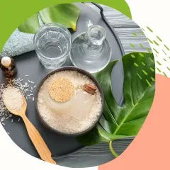 Naturalne składniki do pielęgnacji włosów: ryż i goździki w buteleczkach, woda, ręcznik i liście monstery.