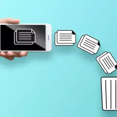 Dłoń trzyma smartfon, z którego ikony dokumentów lecą do kosza. Dowiedz się, jak przywrócić usunięte pliki z kosza.