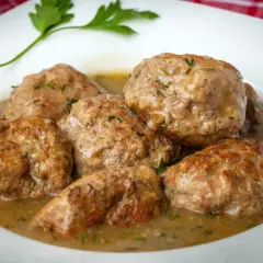 Zrazy z mięsa mielonego w sosie własnym, polane sosem i posypane ziołami, na białym talerzu.