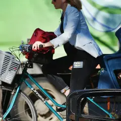 Kobieta w jasnej marynarce i czarnych spodniach z naszywką Batmana jedzie na rowerze. Velo Poprad to jej środek transportu.