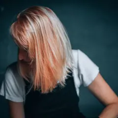 Kobieta z włosami w odcieniu brzoskwiniowy blond, spogląda w dół.