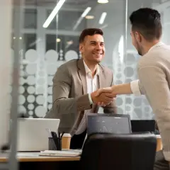 Dwóch mężczyzn w biurze ściska sobie dłonie. Jeden w garniturze, drugi w swetrze. Rozmowa o tym, resell co to, zakończona sukcesem.