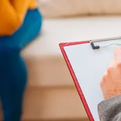 Seduta in terapia, con un professionista che prende appunti. Un passo verso il benessere, forse un giorno con assicurazione psicologi obbligatoria.