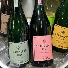 Butelki z napojem typu wino cava, schłodzone w lodzie. Etykiety w kolorach zielonym, różowym i żółtym, z napisem "Sparkling Tea".