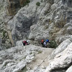Dwóch wspinaczy pokonuje trudną trasę na ferratach w Dolomitach, korzystając z liny asekuracyjnej.