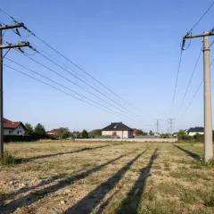 Pusta działka z linią energetyczną przecinającą ją. W tle widać domy mieszkalne.