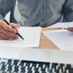 Dłoń z długopisem nad dokumentem, obok laptop. Analiza dokumentacji, być może związanej z art. 674 kodeksu cywilnego.