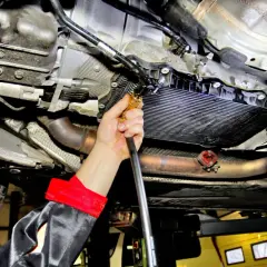Mechanik wykonuje wymianę oleju w skrzyni automatycznej, podłączając wężyk do układu.