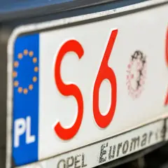Zbliżenie na polskie tablice rejestracyjne z czerwonymi znakami. Widoczne litery "S6" i cyfry "932".