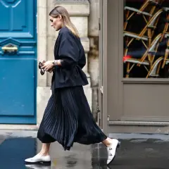 Elegancka kobieta w czarnej, długiej plisowanej spódnicy i marynarce, z białe mokasyny. Inspiracja, jak nosić długą plisowaną spódnicę.
