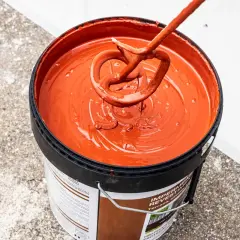 Mezclando pintura impermeabilizante naranja en un cubo. El tiempo secado pintura impermeabilizante es clave para un buen acabado.