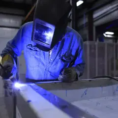 Spawanie aluminium migomatem. Pracownik w masce spawalniczej łączy metalowe elementy, tworząc jasny łuk.
