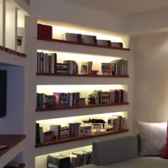 Libreria cartongesso angolare con illuminazione integrata, piena di libri e oggetti decorativi.