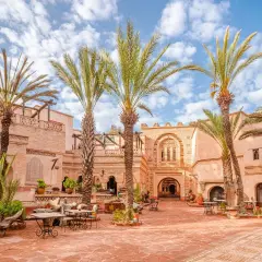 Sonniger Innenhof in der Agadir Altstadt mit Palmen, traditioneller Architektur und Sitzgelegenheiten im Freien.
