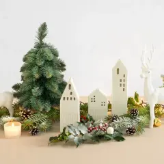 Bożonarodzeniowa dekoracja: białe renifery, choinka, ceramiczne domki, lampki i szyszki.