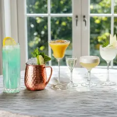 Fem olika vodka drinkar, från en blå long drink till en gyllene passionfruktscocktail och en vit äppeldryck, står uppradade på ett dukat bord.