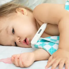 Bambino con termometro sotto l'ascella, avvolto in un asciugamano a quadri. La febbre che non scende bambini è una preoccupazione.