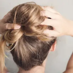 Hände formen einen unordentlichen Dutt, eine von vielen leichten Frisuren für den Alltag.