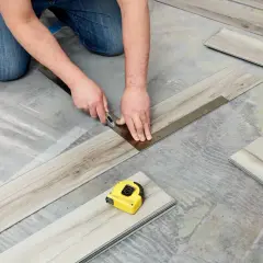 A person is cutting vinyl plank flooring that is not laying flat during installation. A tape measure is nearby.