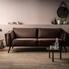 Elegancka kanapa w odcieniu barwy brązowej, obok stolik z lampką i dekoracjami.
