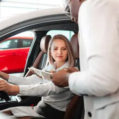 Kobieta za kierownicą nowego auta, sprzedawca omawia warunki fiat leasing.