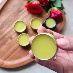 Małe, złote pojemniczki z zielonym balsamem, idealne do domowej produkcji perfum. Różane akcenty dodają uroku.
