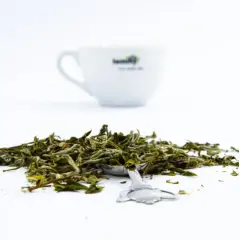 Suszone liście białej herbaty na łyżeczce, w tle biała filiżanka. Odkryj niezwykłe biała herbata właściwości.