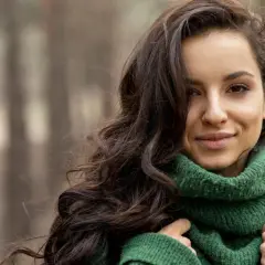 Brunetka w zielonym swetrze, idealne kolory dla brunetek. Jej ciemne włosy falują na wietrze, a uśmiech rozjaśnia twarz.
