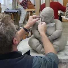 Ein Künstler formt mit Werkzeug eine Tonfigur in einem Atelier.