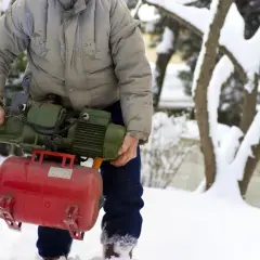 Mężczyzna w zimowej scenerii trzyma pompę, przygotowując się do zadania, jak wypompować wodę ze zbiornika na deszczówkę.