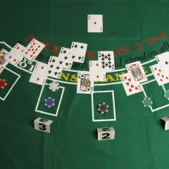 Kier karty na zielonym stole do blackjacka. Widoczne karty, żetony i kostki z numerami.