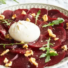 Rote Bete Carpaccio italienisch mit Burrata, Walnüssen und Rucola auf einem Teller.