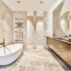 Elegantes, fugenloses Bad mit freistehender Wanne, Marmorwänden und einem langen Waschtisch mit Spiegel.