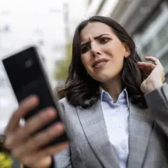 Zmartwiona kobieta próbuje odzyskać hasło do FB, patrząc na telefon.