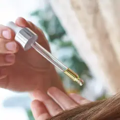 Kropla olejku rycynowego na włosy, aplikowana pipetką, by nadać im blask i wzmocnić.