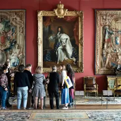 Visiteurs admirant le portrait de Louis XIV et des tapisseries grandioses, une scène digne des 50 plus beaux tableaux du Louvre.