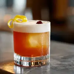 En Amaretto Sour med skummig topp, citronskal och körsbär. Perfekt för en mysig kväll.