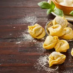 Pyszne tortellini na obiad, posypane mąką, obok świeżej bazylii i kulek mozzarelli.