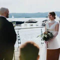 Panna młoda w białej sukni i welonie, z bukietem kwiatów, słucha przysięgi podczas ślubu jednostronnego nad jeziorem.