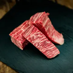 Drei Stücke erstklassiges Kobe Rindfleisch mit feiner Marmorierung liegen auf einem dunklen Stein.
